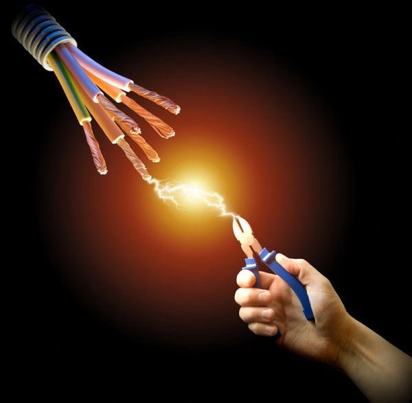Hand with pliers touching live electrical wires sparking.
