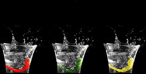 Three glasses with colorful liquid splashes against black background.